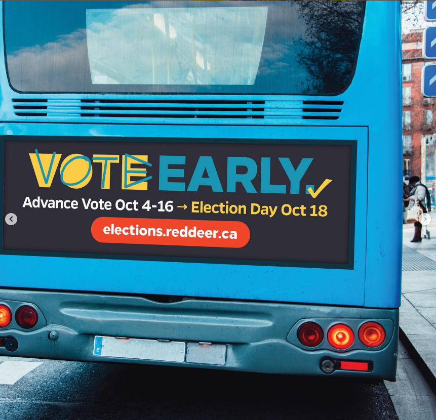 The rear of a city transit bus displaying a large election advertisement for the City of Red Deer 2021 Election. The ad reads “Vote Early” in bold teal and yellow lettering, followed by “Advance Vote Oct 4–16 → Election Day Oct 18.” A red pill shaped button displays the website “elections.reddeer.ca.” The graphic uses a dark background with bright, high contrast text and checkmark icons for visibility. The bus is stopped on a city street, with buildings and pedestrians visible in the background.
