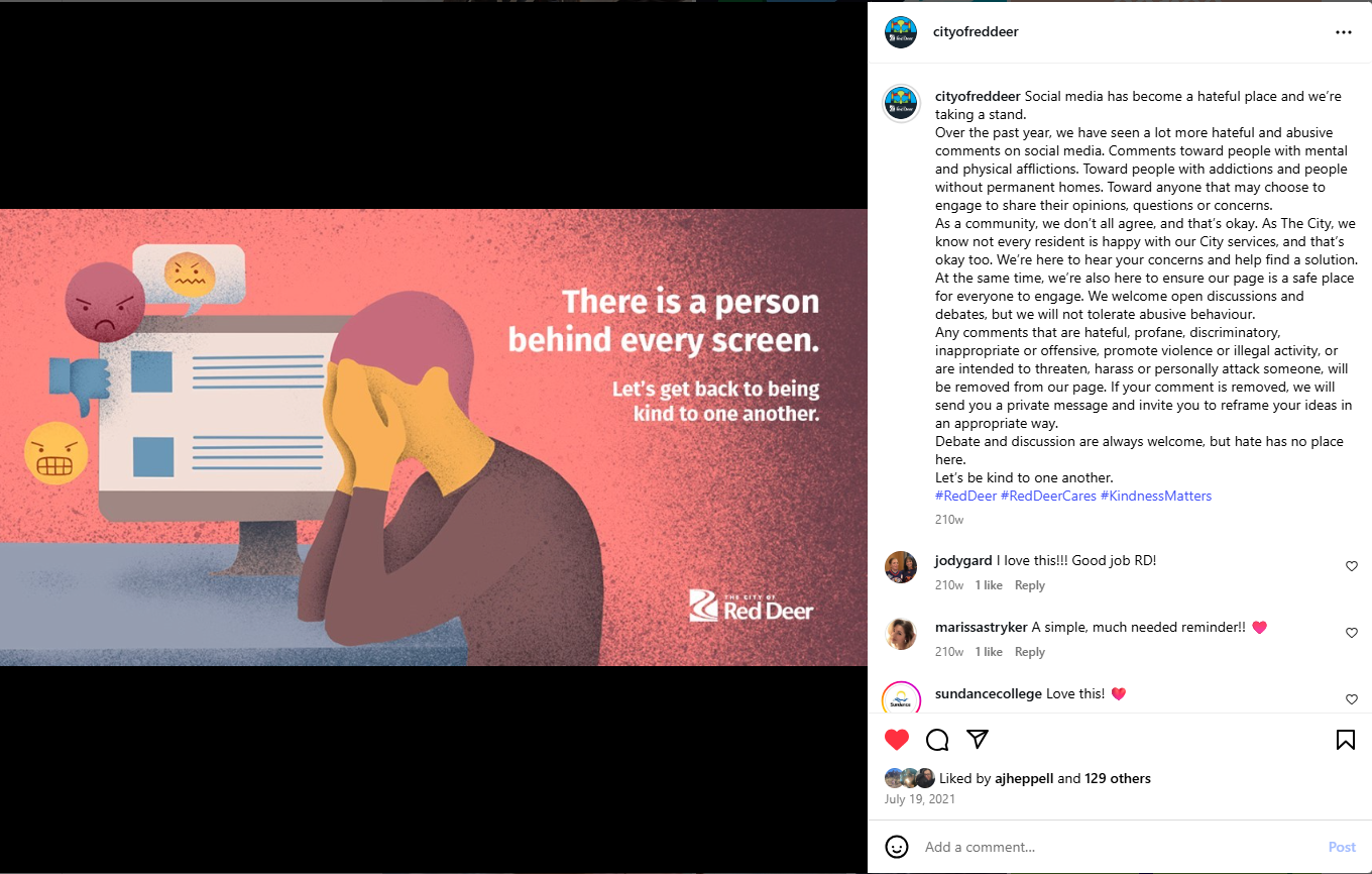 A screenshot of a City of Red Deer Instagram post with an illustrated graphic on a red‑to‑pink gradient background. The illustration depicts a person seated at a computer, with multiple comment bubbles and negative reaction icons displayed on the screen and nearby. White text reads, “There is a person behind every screen. Let’s get back to being kind to one another.” The City of Red Deer logo appears in the lower right corner. The accompanying caption outlines expectations for respectful discussion and moderation on the City’s social media channels.