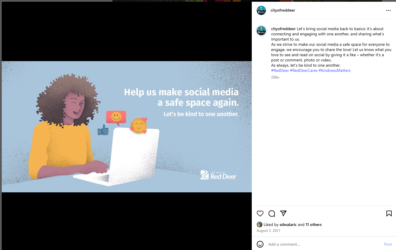 A screenshot of a City of Red Deer Instagram post featuring an illustrated graphic on a light blue background. The illustration shows a person seated at a laptop, with floating social media reaction icons such as thumbs‑up and smiling faces near the screen. White text reads, “Help us make social media a safe space again. Let’s be kind to one another.” The City of Red Deer logo appears in the bottom right corner. The post caption beside the image discusses encouraging positive engagement and kindness on social media.
